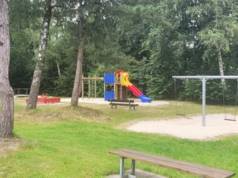 3_kcp_haren_Spieleparadies.jpg Spielplatz mit Rutsche, Schaukeln und Sandkasten zwischen Bäumen im grünen Bereich des Campingparks.