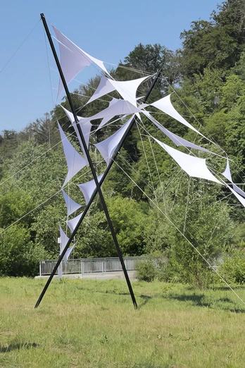 Das Kunstwerk Brückenschlag von Jens J. Meyer auf den Skulpturenwege Langenberg Weiße Segel aus Stoff, aufgespannt auf Metallstäben, stehen vor einem Wald am Skulpturenweg.