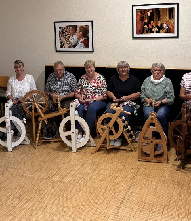 Einmal im Monat trifft sich die Handspinner-Gruppe in Emsbüren Gruppe von Menschen sitzt lachend mit Spinnrädern in einem Raum und spinnt gemeinsam Wolle.