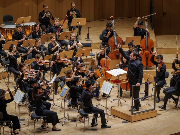 Moritzburg Festival Akademie © Oliver Killig.JPG Musiker spielen in einem Konzertsaal, dirigiert von einem Dirigenten; klassische Musikaufführung.