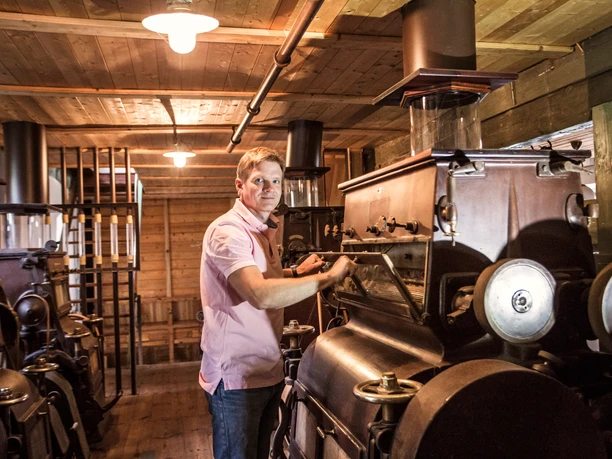 _L3A0699_1.jpg Ein Mann bedient historische Maschinen in einer holzgetäfelten Werkstatt.