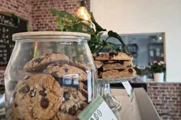 zuckerschmiede.jpg Ein Café mit rustikaler Backsteinwand, Cookies im Glas und Schokotörtchen auf einem Teller.