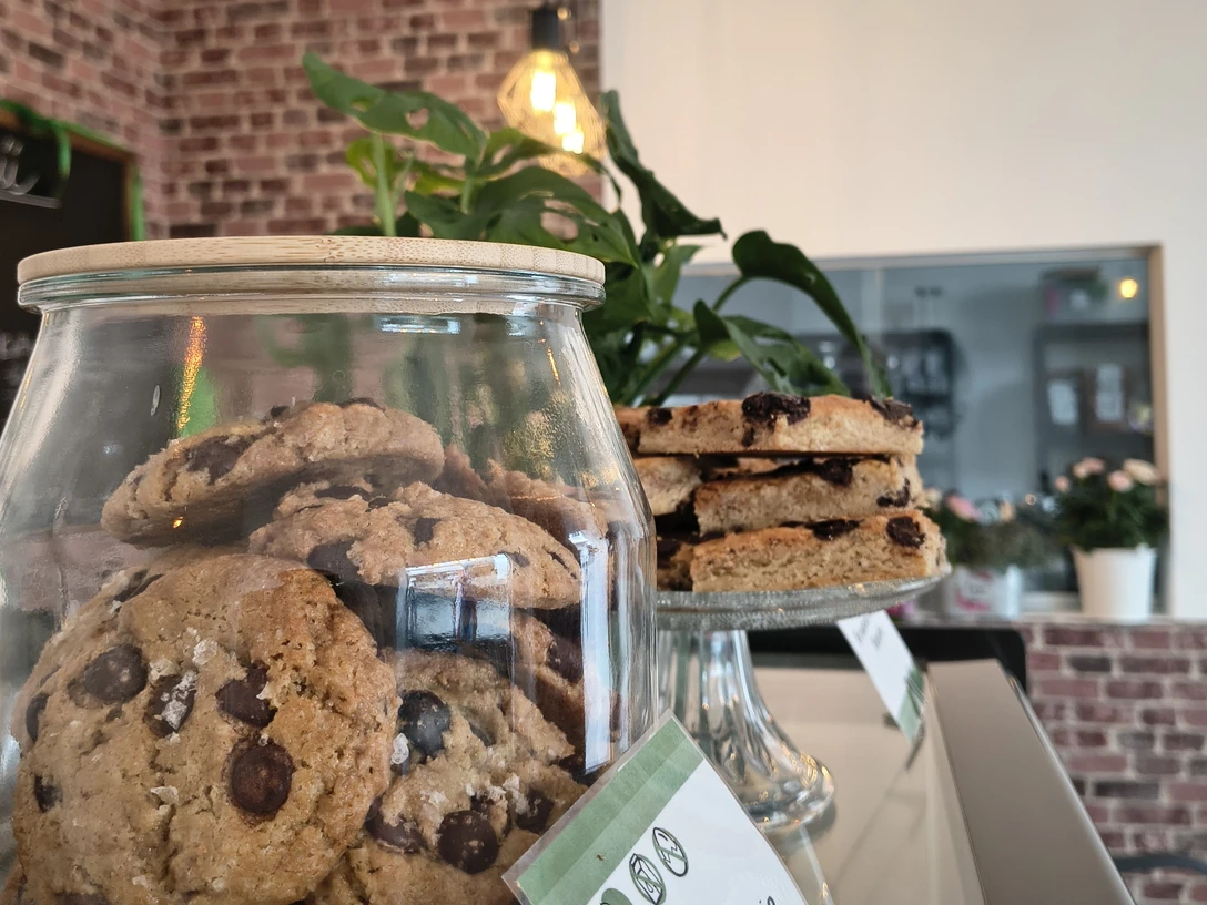 zuckerschmiede.jpg Ein Café mit rustikaler Backsteinwand, Cookies im Glas und Schokotörtchen auf einem Teller.