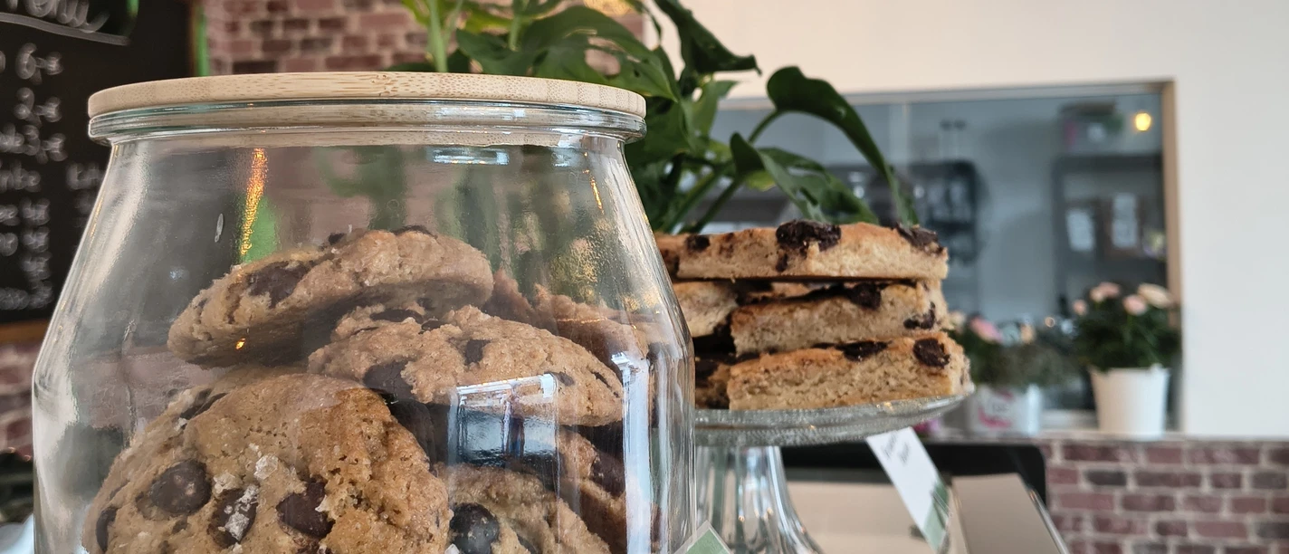 zuckerschmiede.jpg Ein Café mit rustikaler Backsteinwand, Cookies im Glas und Schokotörtchen auf einem Teller.