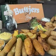 Buttjers Bar_1.jpg Eine Auswahl an frittierten Snacks und Saucen neben Gastrokarten, präsentiert auf einem Tisch.
