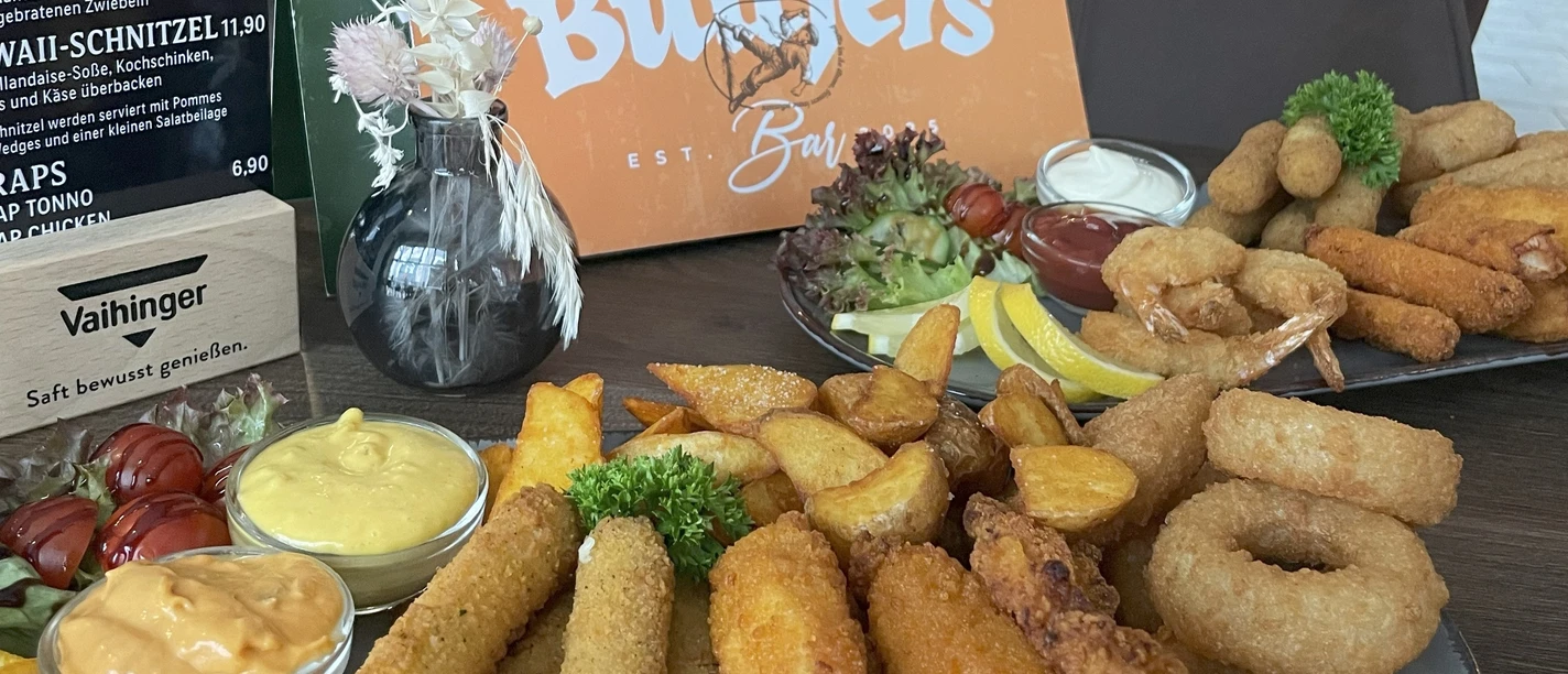 Buttjers Bar_1.jpg Eine Auswahl an frittierten Snacks und Saucen neben Gastrokarten, präsentiert auf einem Tisch.