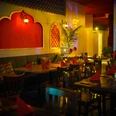 Mandaloun.jpg Innenansicht eines orientalischen Restaurants mit roten Wänden, Holzstühlen und weich beleuchteten Lampen.
