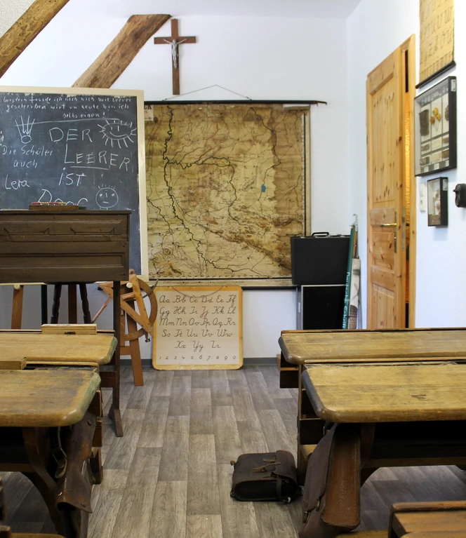 Heimatmuseum Langen – Blick in Klassenzimmer ©Emsland Tourismus GmbH.JPG Historisches Klassenzimmer mit alten Holzschulbänken, Kreidetafel, Karte und Kreuz an der Wand