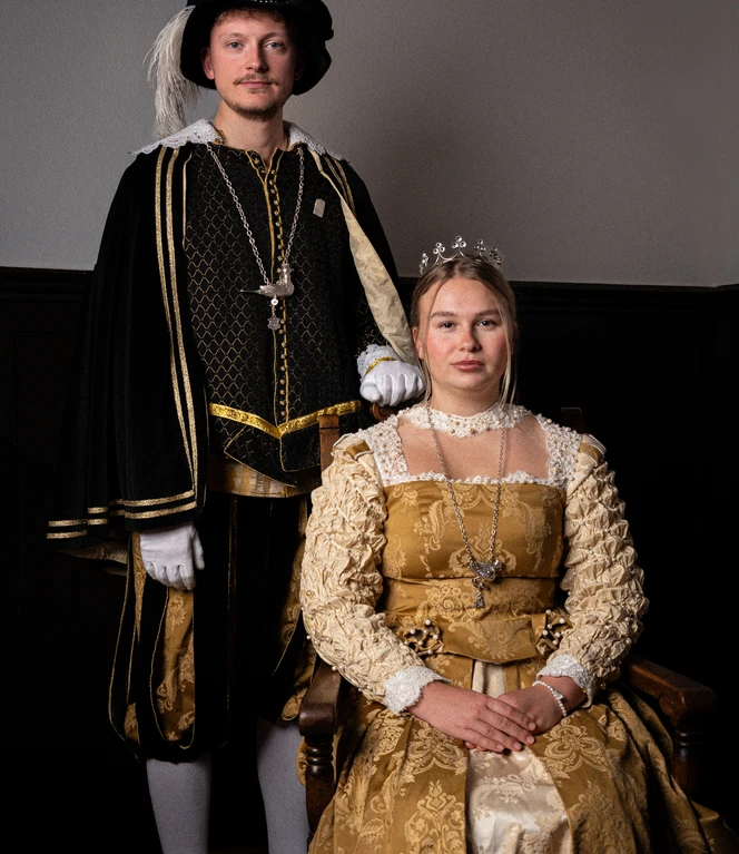 Königspaar der Kivelinge in Lingen - Fynn Bosse und Flora Hofschröer ©Die Kivelinge e.V.JPG Ein Paar in historischen Kostümen der Renaissancezeit posiert in festlicher Haltung vor dunkler Wand.