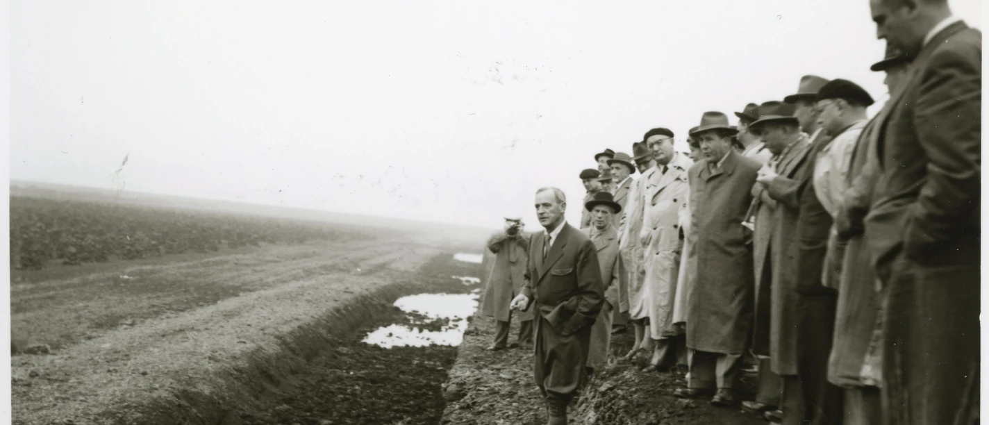 1 ©Kreisarchiv Emsland.jpg Gruppe von Männern in Anzügen und Mänteln betrachtet einen Entwässerungsgraben im Moorgebiet.