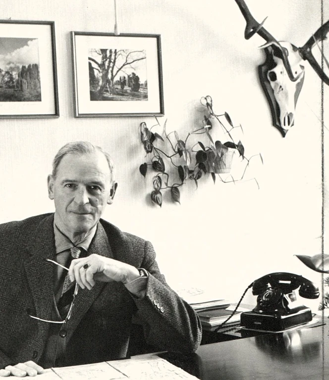 Johann Dietrich Lauenstein – 1. GF der Emsland GmbH_bearbeitet ©Emsländischer Heimatbund e.V..jpg Älterer Mann im Anzug sitzt an einem Schreibtisch mit Telefon, Pflanzen und gerahmten Bildern an der Wand.