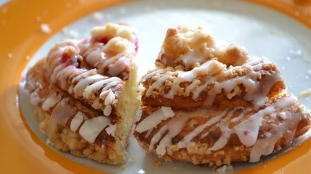 Zwei Scheiben Kuchen mit Streuseln und Zuckerguss auf orangefarbenem Teller.