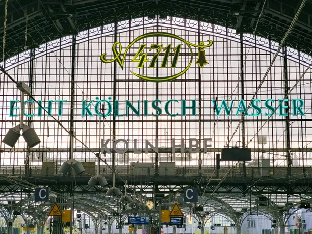 Köln Hauptbahnhof Das Bild zeigt die Glashalle des Kölner Hauptbahnhofs mit dem markanten "4711 Echt Kölnisch Wasser"-Schriftzug. Im Hintergrund sind architektonische Details der Bahnhofskonstruktion sichtbar.