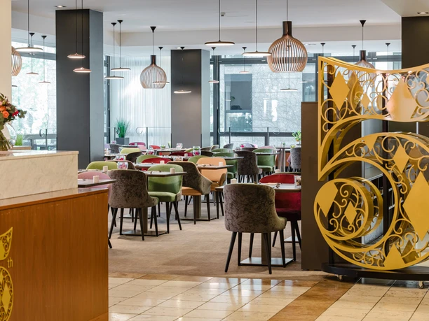 MGallery_Koeln166.jpg Eleganter Restaurantbereich mit modernen, farbenfrohen Sitzmöbeln und kunstvollen Dekorationselementen.