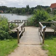 Landangelstelle Schulsee Mölln_barrierearm Holzplattform am Schulsee umgeben von Schilf und Bäumen, geeignet für Angler und Personen mit Mobilitätseinschränkungen am ruhigen Wasser.
