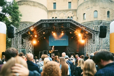 gamescom city festival A guitar player performs on an outdoor stage, surrounded by an audience in front of a historic fortress.