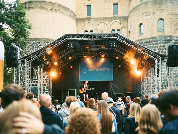 gamescom city festival A guitar player performs on an outdoor stage, surrounded by an audience in front of a historic fortress.