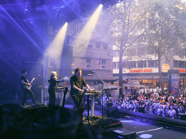 gamescom city festival Blick von der Bühne auf drei Musiker bei einem Konzert vor großem, begeistertem Publikum im Freien.