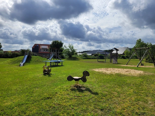 Spielplatz in Bispingen am Drögenberg mit Schaukel, Rutsche, Sandkasten und Wippe auf grünem Rasen unter blauen Himmel