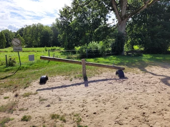 Badeteich_Steinbeck__02.jpg Holz-Wippe auf Sandfläche am Badeteich Steinbeck, umgeben von grünen Bäumen und Wiesen
