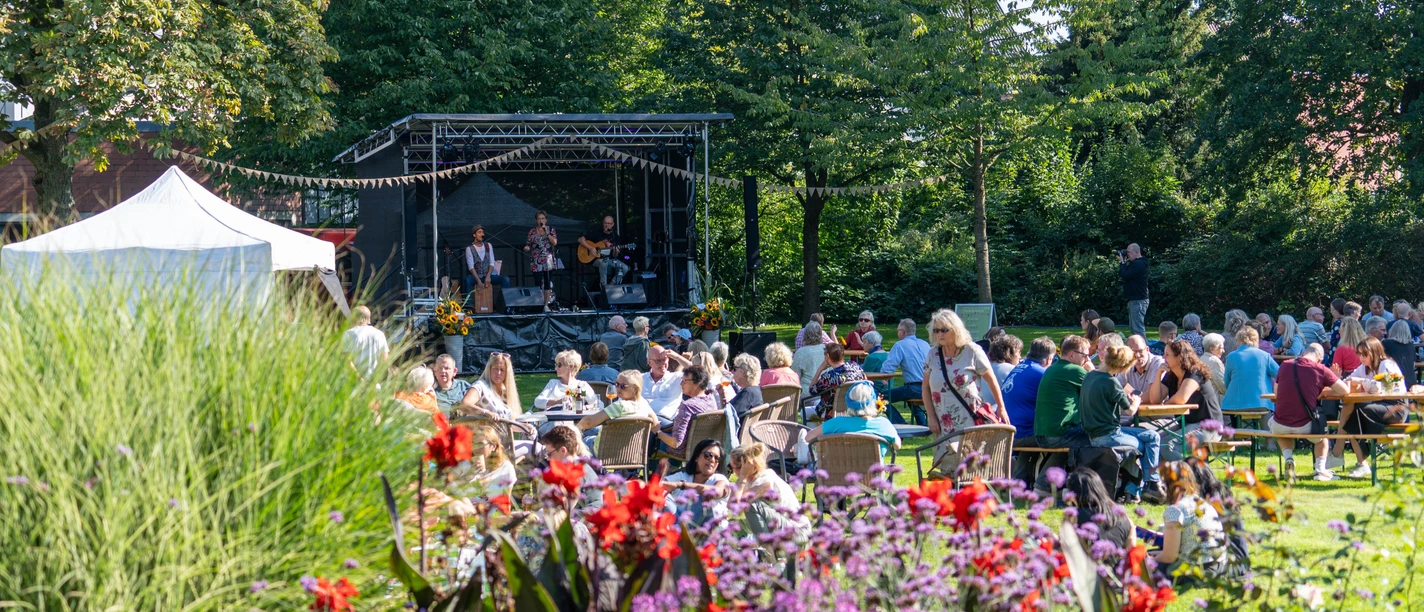 Spätsommerkonzert Open-air concert in the countryside with musicians on stage and audience at tables in the sunshine.