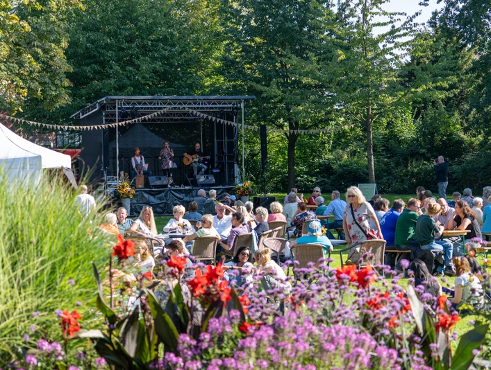 Spätsommerkonzert Open-Air-Konzert im Grünen mit Musikern auf Bühne und Publikum an Tischen im Sonnenschein.