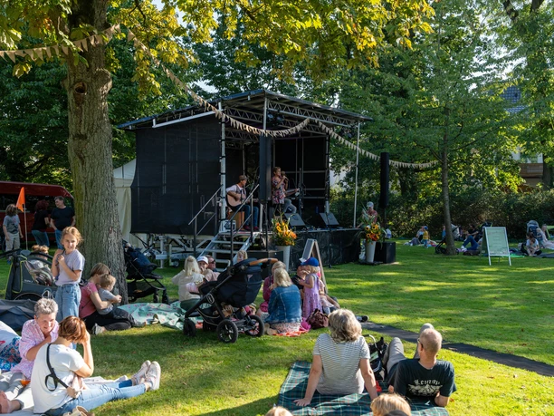 Spätsommerkonzert_Stadt Melle_Foto Sebastian Hummel.jpg People sit on picnic blankets on a meadow in front of an outdoor stage.
