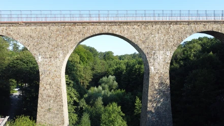 Saubrücke Velbert 01_Stadtmarketing Velbert.JPG Eine imposante Steinbrücke mit drei Bögen überspannt einen üppig bewachsenen Wald in Velbert.