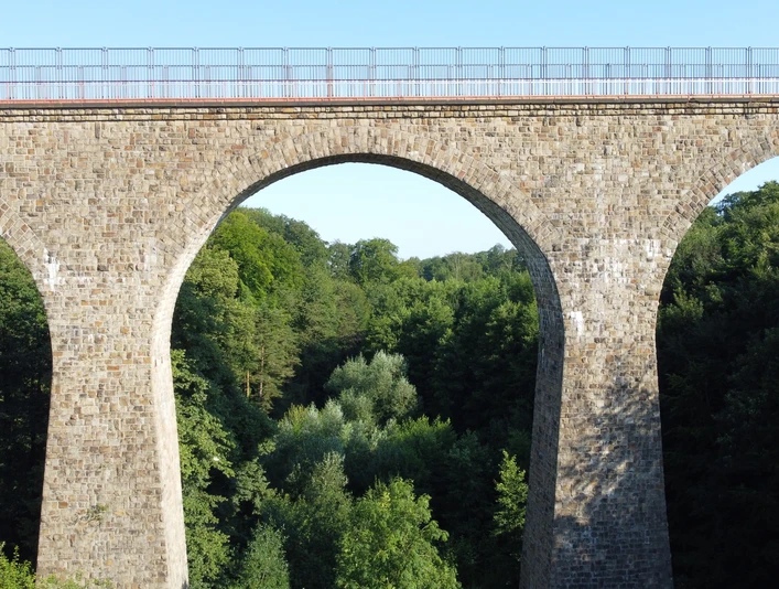 Saubrücke Velbert 01_Stadtmarketing Velbert.JPG Eine imposante Steinbrücke mit drei Bögen überspannt einen üppig bewachsenen Wald in Velbert.