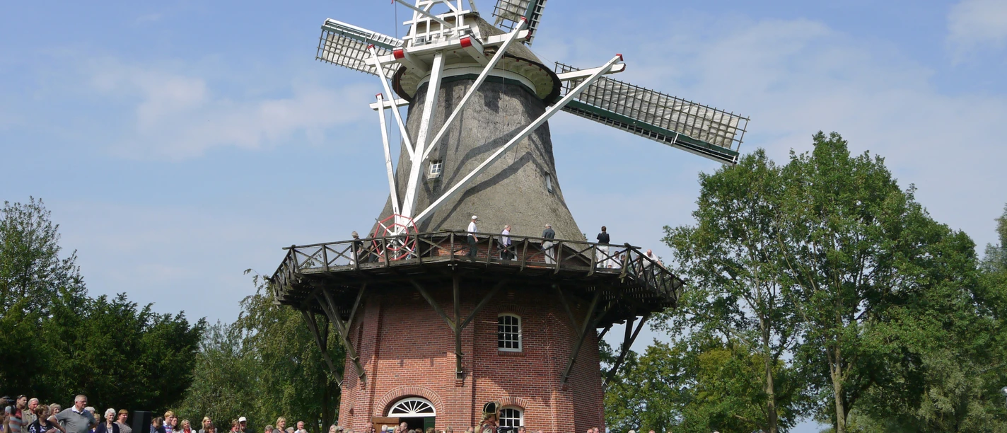 tag-der-heimat-bei-der-muehle.jpg People in traditional costumes gather in front of a historic mill for a celebration.