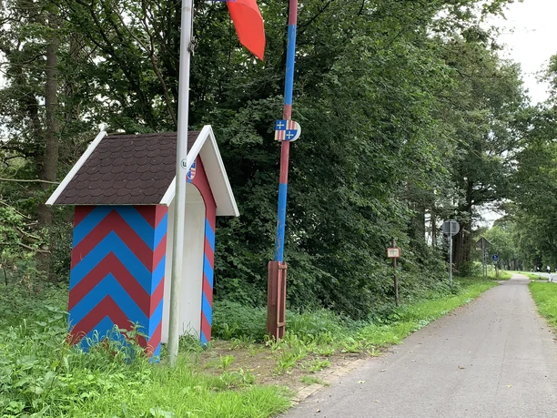 Grenzstation Holtgast Rot-blau gestreifte Grenzstation an einem von Bäumen gesäumten Weg.