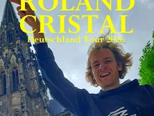 Ein junger Mann mit blondem Haar vor einer gotischen Kathedrale, zeigt auf etwas in der Ferne.