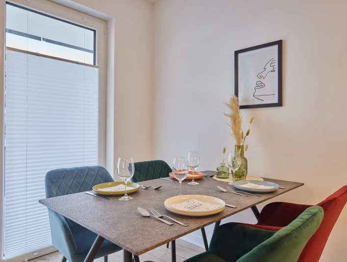 Esstisch Ein moderner Esstisch mit farbenfrohen Stühlen, gedeckt mit Gläsern und Tellern für vier Personen.