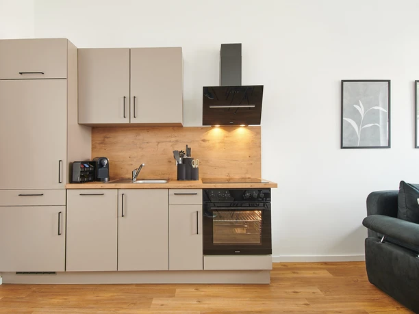 Küchenzeile Moderne Küchenzeile mit beige Schränken, Holzarbeitsplatte, Herd und Dunstabzug, daneben ein Sofa.