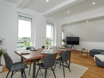 Wohn-/Essbereich Moderner Wohn- und Essbereich mit Esstisch, schwarzen Stühlen und Ecksofa in hellem, lichtdurchflutetem Raum.