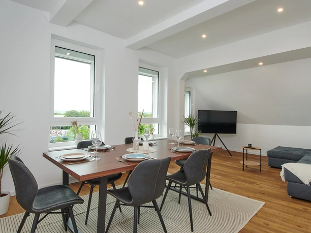 Wohn-/Essbereich Moderner Wohn- und Essbereich mit Esstisch, schwarzen Stühlen und Ecksofa in hellem, lichtdurchflutetem Raum.