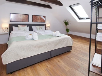 Schlafzimmer Dachgeschoss-Schlafzimmer mit Doppelbett, Holzboden, Dachfenster und dekorativen Bildern an der Wand.