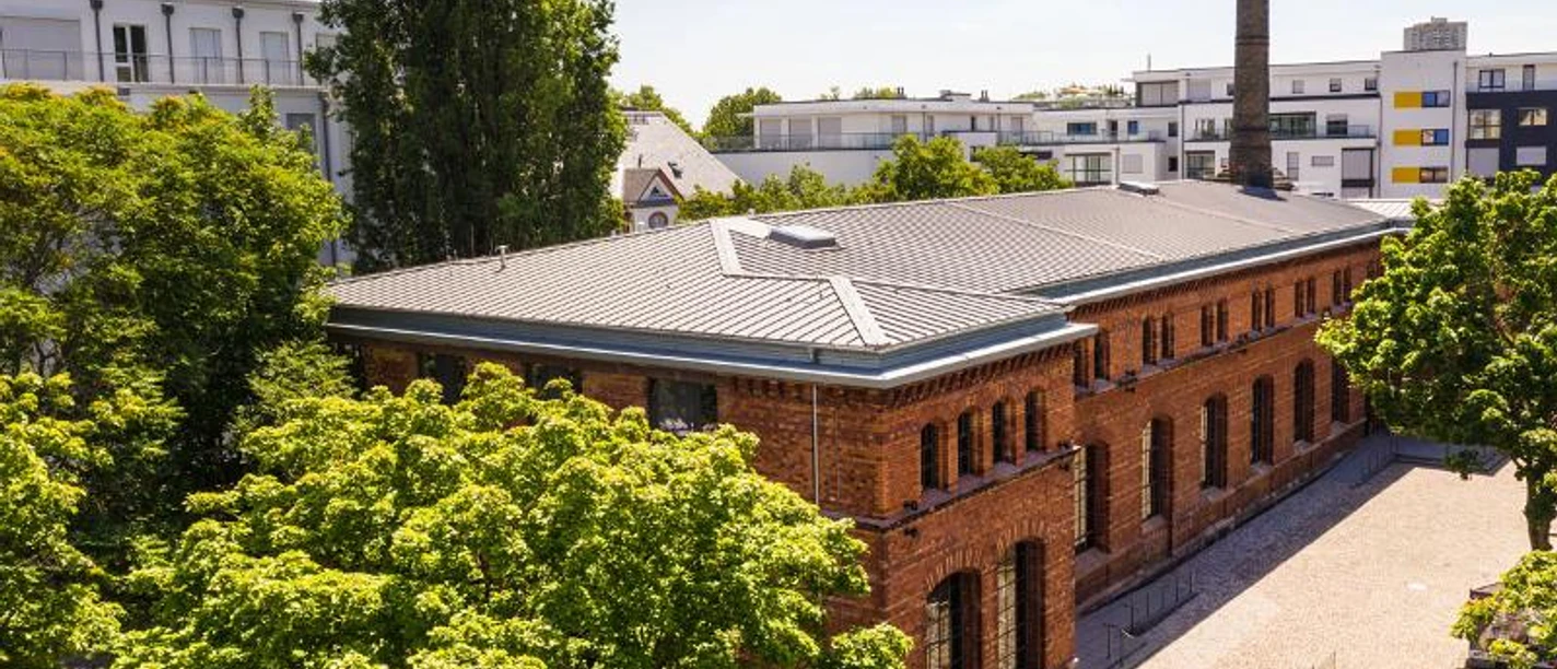 KUZ - Kulturzentrum Mainz KUZ Mainz: Backsteingebäude mit hohem Schornstein, umgeben von Bäumen und Gebäuden.