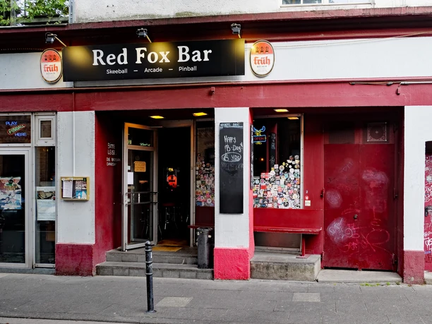 Red Fox Bar Der Eingangsbereich der Red Fox Bar in Köln, umgeben von roten Wänden und Stickern.