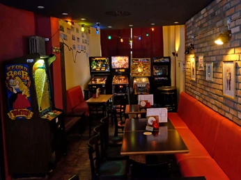 Gaming and pinball machines in the Red Fox Bar Das Bild zeigt eine Bar mit dunklem Holzmobiliar, roten Sitzbänken und mehreren Flipperautomaten an der Wand. Bunte Lichterketten hängen von der Decke, während an den Wänden verschiedene Bilder und Retro-Dekorationen zu sehen sind.The picture shows a bar with dark wooden furniture, red benches and several pinball machines on the wall. Colorful fairy lights hang from the ceiling, while various pictures and retro decorations can be seen on the walls.