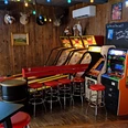 Skeeball- und Arcade-Spiele in der Red Fox Bar Eine rustikale Bar mit Holzwänden, Arcade-Spielen, roten Barhockern und entspannter Atmosphäre.A rustic bar with wooden walls, arcade games, red bar stools and a relaxed atmosphere.