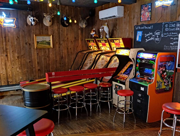 Skeeball- und Arcade-Spiele in der Red Fox Bar Eine rustikale Bar mit Holzwänden, Arcade-Spielen, roten Barhockern und entspannter Atmosphäre.A rustic bar with wooden walls, arcade games, red bar stools and a relaxed atmosphere.