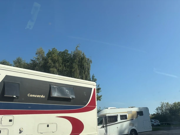 Wohnmobile - Wohnmobilstellplatz am Sportzentrum Hasetal Zwei große Wohnmobile stehen nebeneinander auf einem sonnigen Stellplatz mit klarem blauen Himmel.