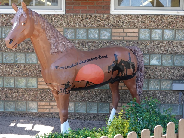 Bruin paardenfiguurtje met een zonsondergangmotief en het opschrift ‘Ferienhof Junkern-Beel’ tegen een gevel