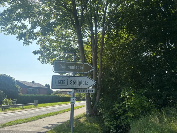 Wegweiser - Wohnmobilstellplatz am Sportzentrum Hasetal Wegweiser an einer Straße mit Schildern zum Bootsanleger, Stellplatz und zu den Tennisanlagen.