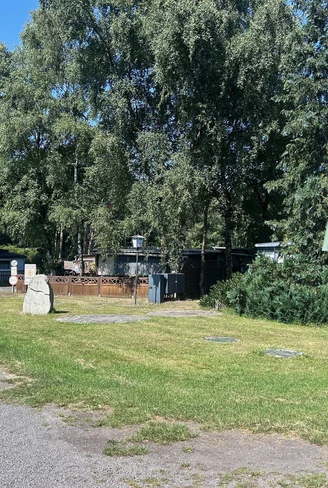 Zufahrt zum Campingplatz mit schattigen Bäumen, Wiesenfläche und Stellplätzen mit Wohnwagen.
