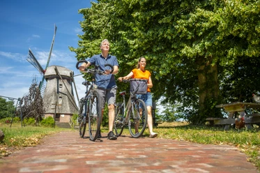 Ein Paar schiebt Fahrräder auf einem Weg vor der Hilter Mühle an einem sonnigen Sommertag.