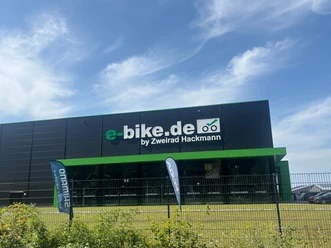 Zweirad Hackmann Modernes Fahrradgeschäft mit großer Glasfront und grün-schwarzer Fassade unter blauem Himmel