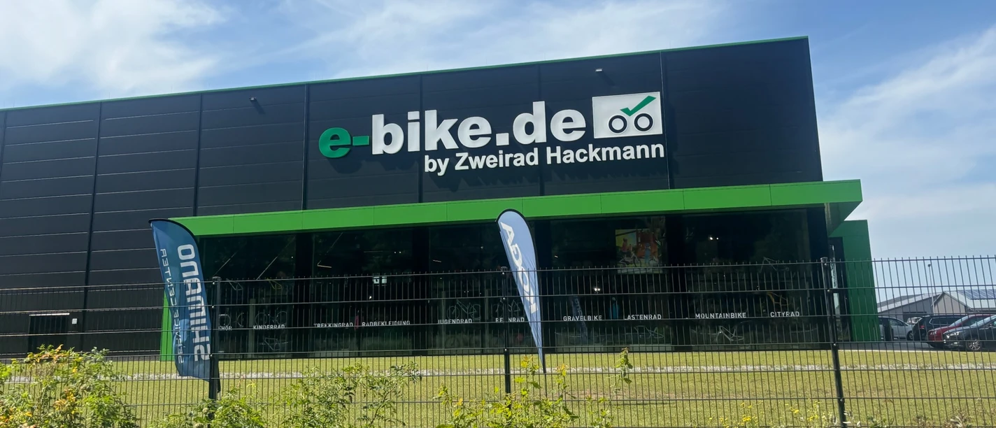 Zweirad Hackmann Modernes Fahrradgeschäft mit großer Glasfront und grün-schwarzer Fassade unter blauem Himmel