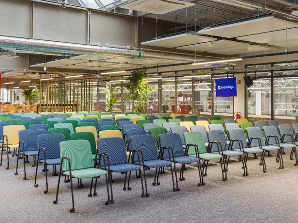 Reihen bestuhlter bunter Stühle in einem modernen, hellen Raum mit industriellen Designelementen.